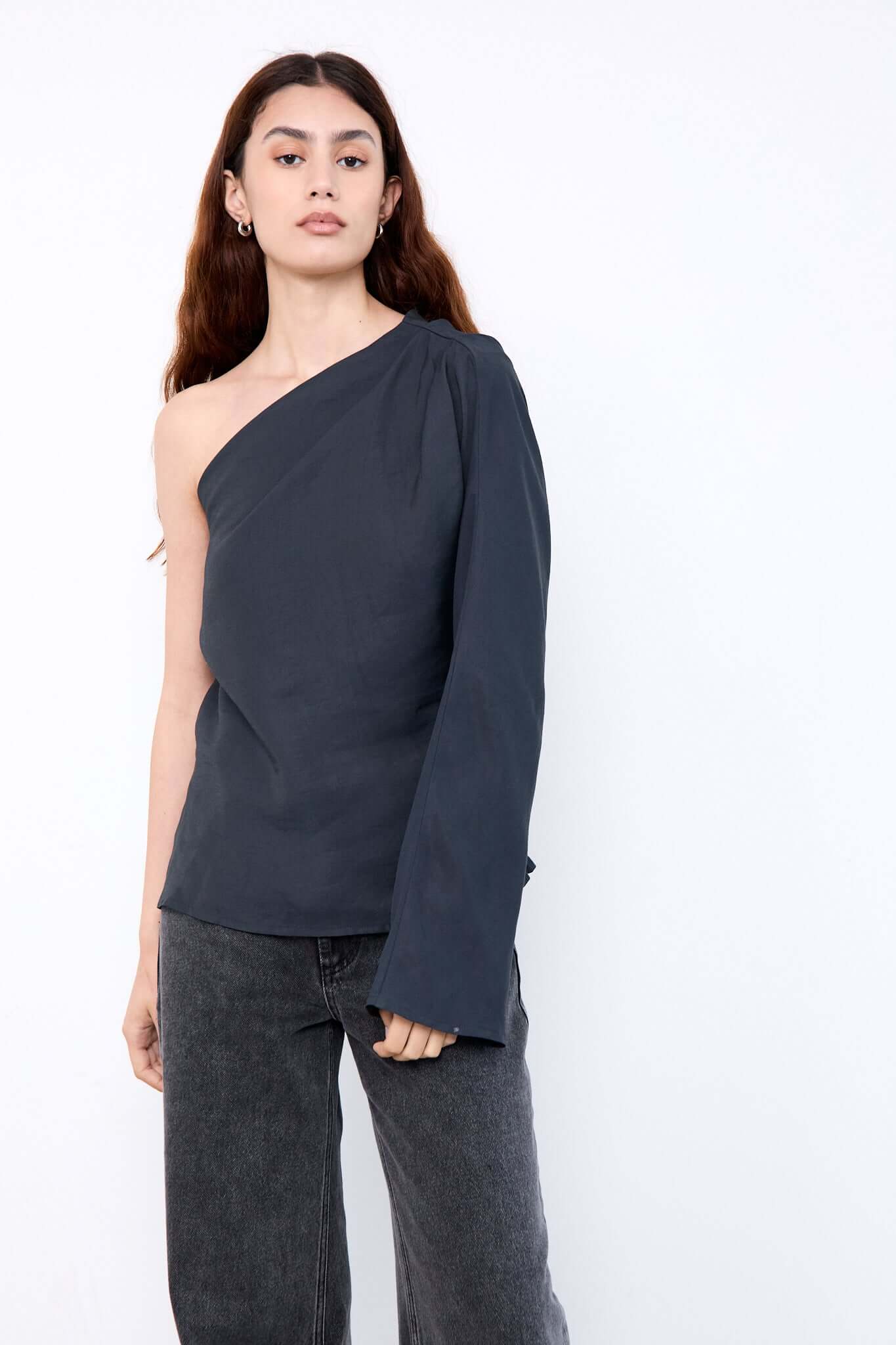 Woman wearing a dark gray one-shoulder top and jeans