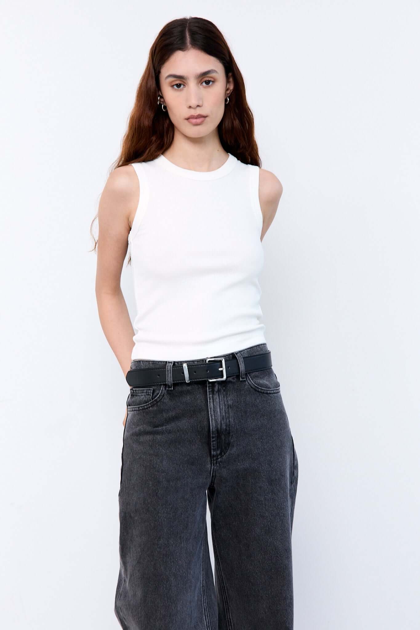 Woman wearing a white sleeveless top and dark jeans