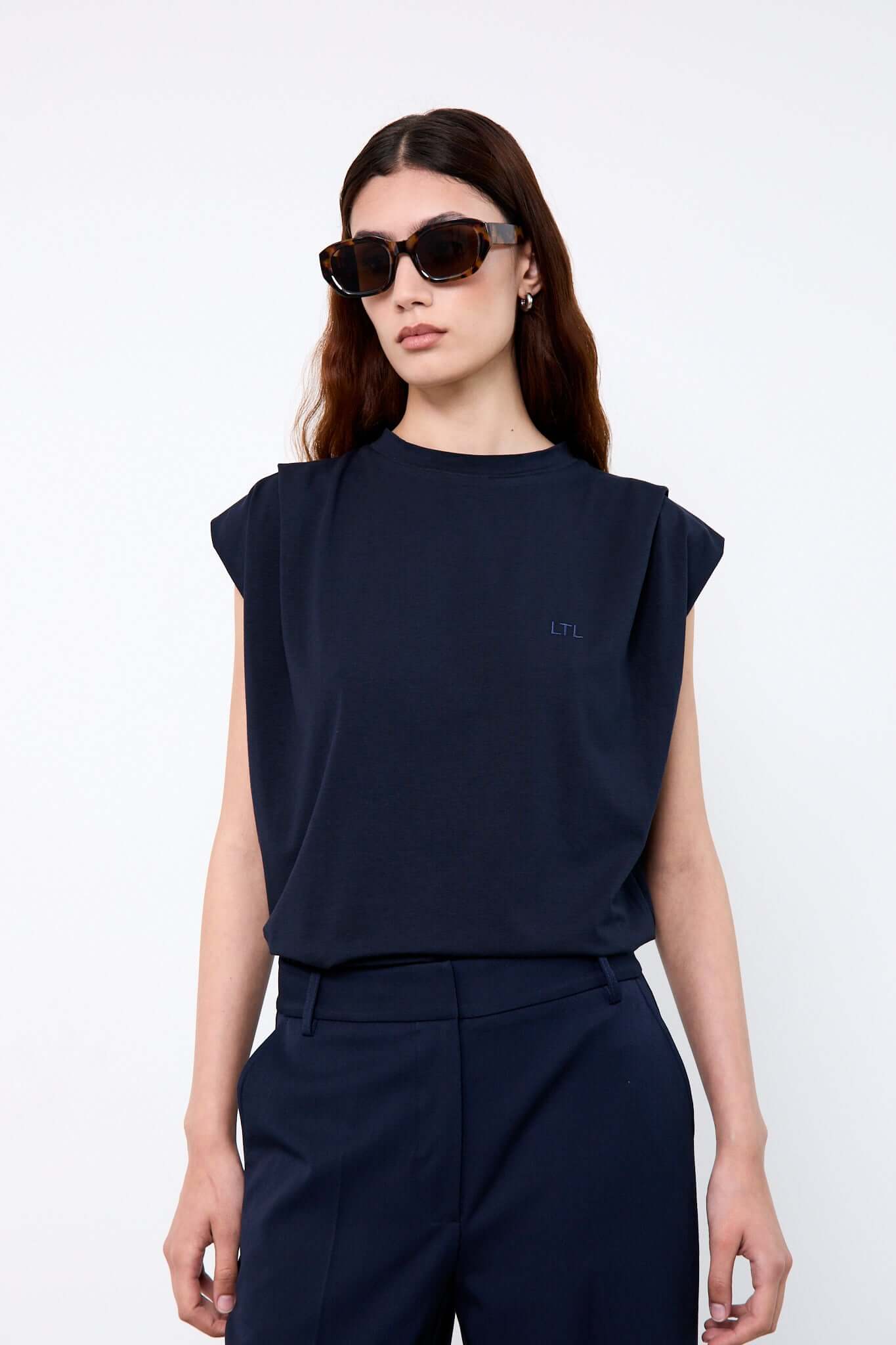 Woman wearing a navy blue sleeveless top and pants with sunglasses