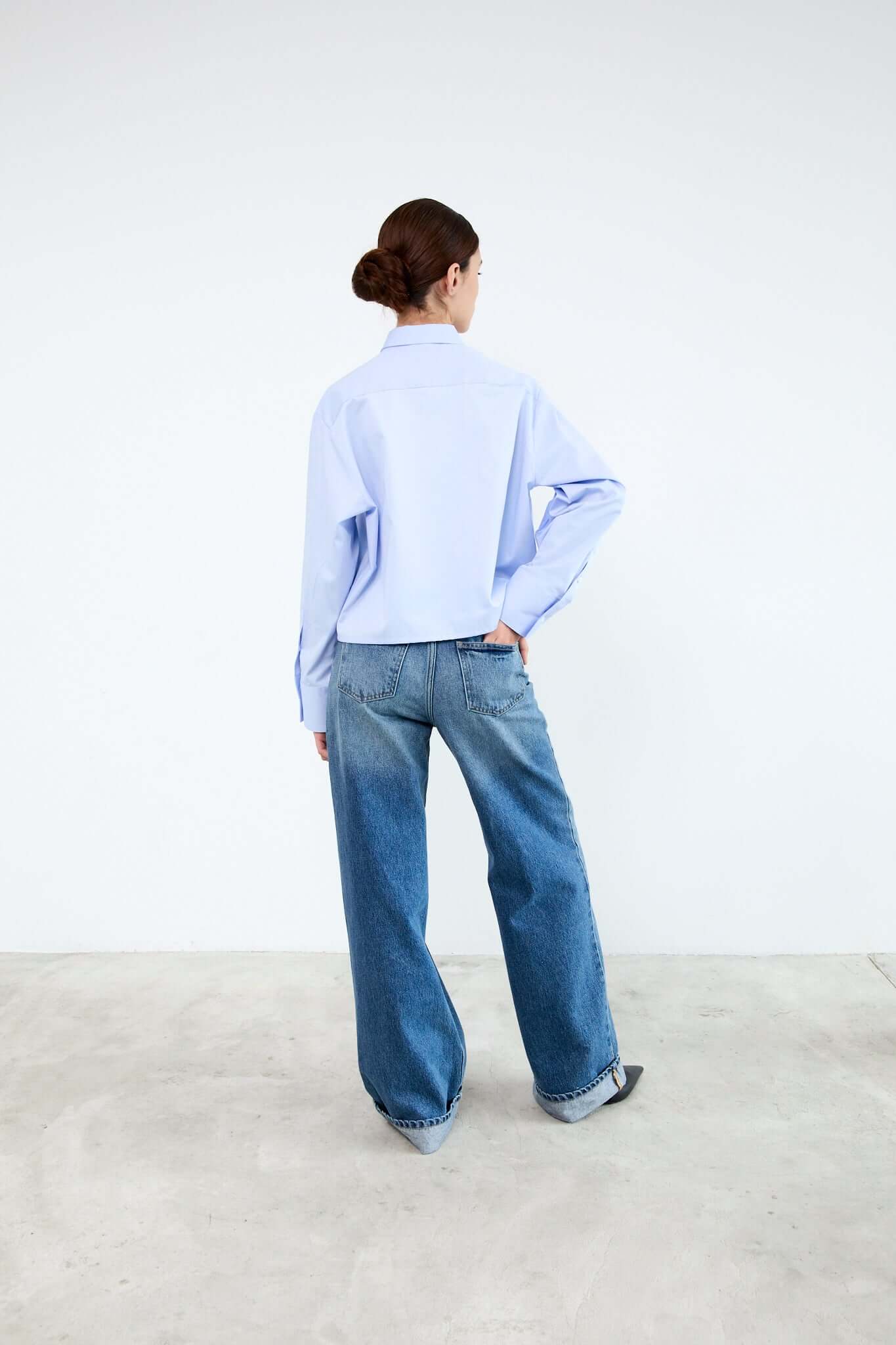Person wearing a light blue shirt and blue jeans standing