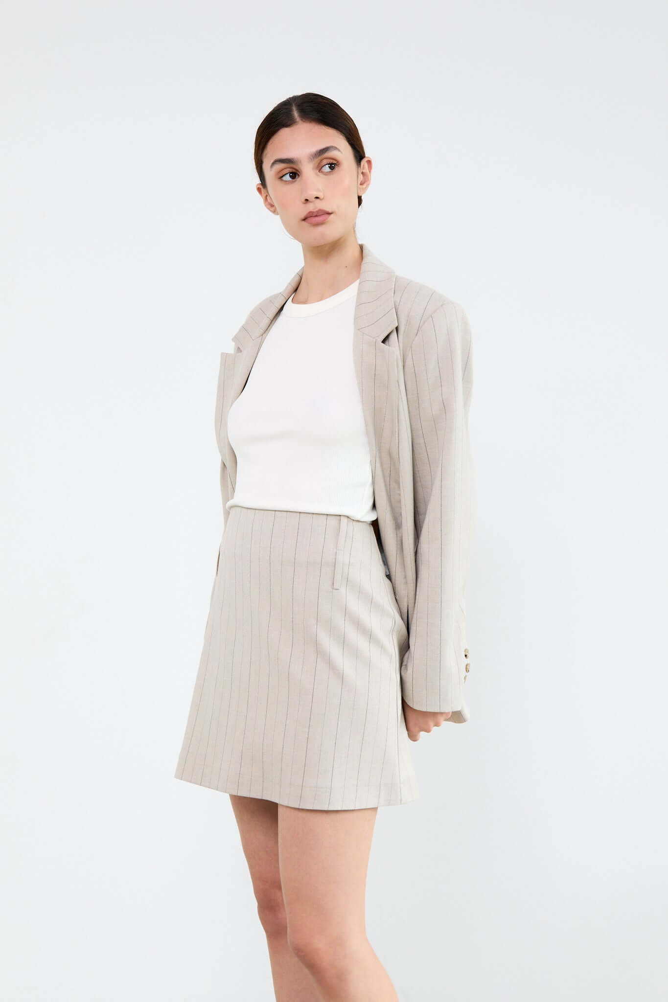 Woman wearing a beige blazer, white top, and beige pinstripe skirt