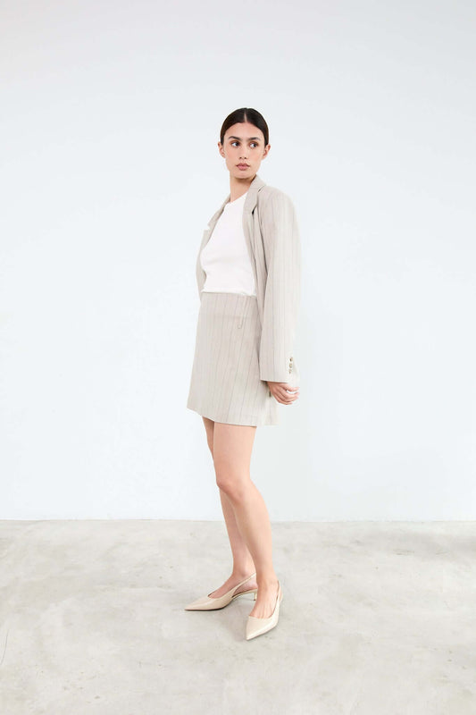 Woman wearing a beige blazer, white top, and skirt with beige shoes
