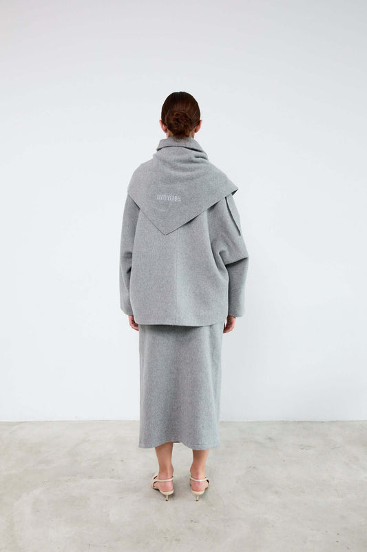 Person wearing a gray coat and skirt set against