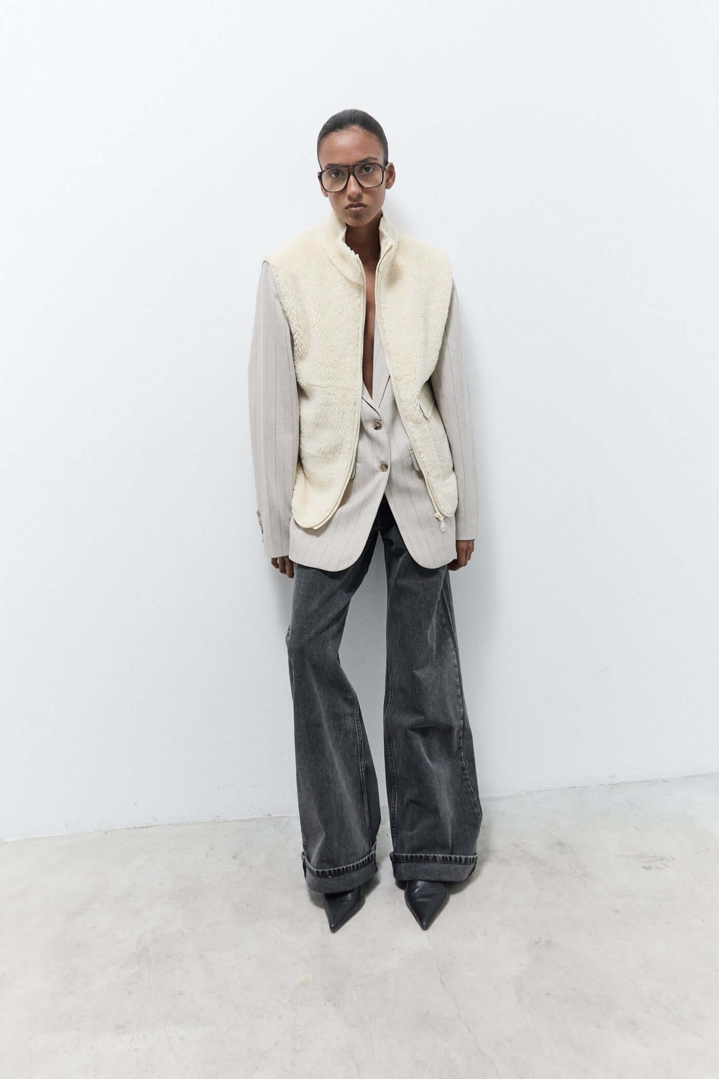 Person wearing a white blazer with fur collar and dark jeans against a white background
