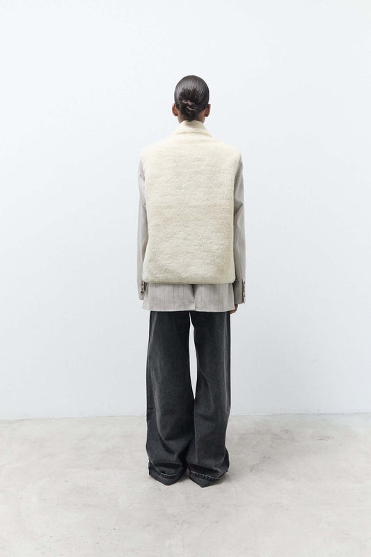 Person wearing a light-colored vest over a gray outfit on a white background