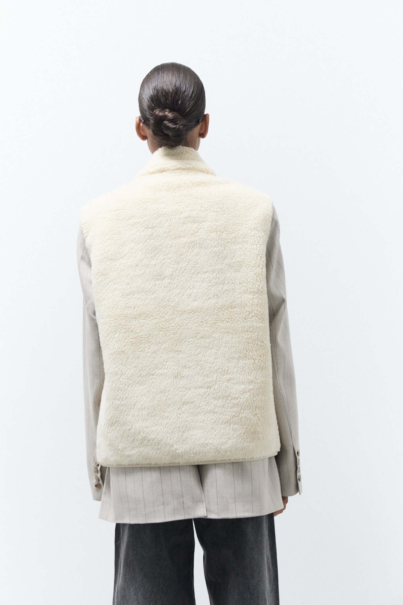Person wearing a light-colored quilted vest over a gray outfit on a white background