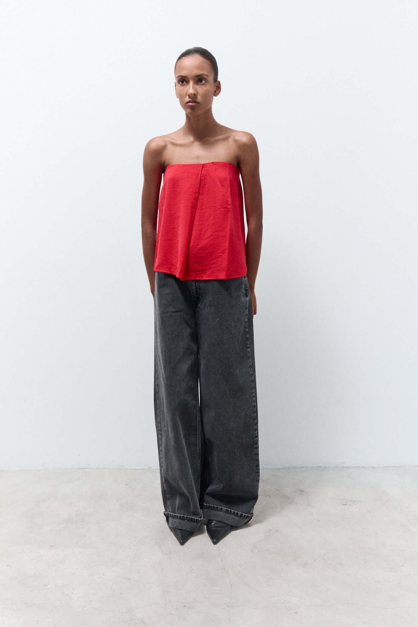 Woman wearing a red strapless top and black wide-leg pants on a white background