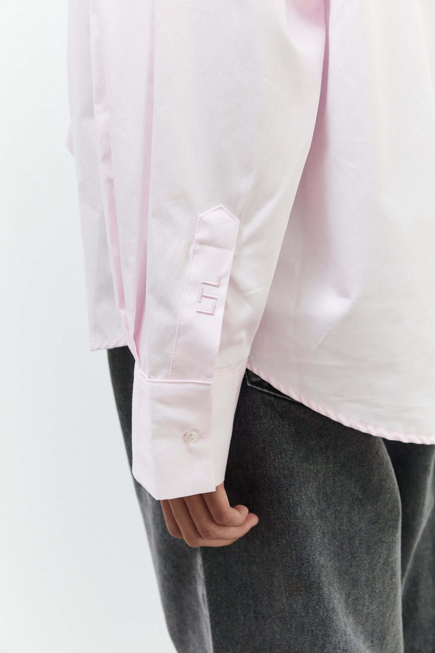 Close-up of a person wearing a light pink shirt and dark gray pants on a white background