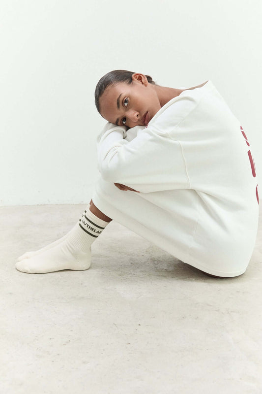 Person sitting on a white floor wearing a white outfit with red text.