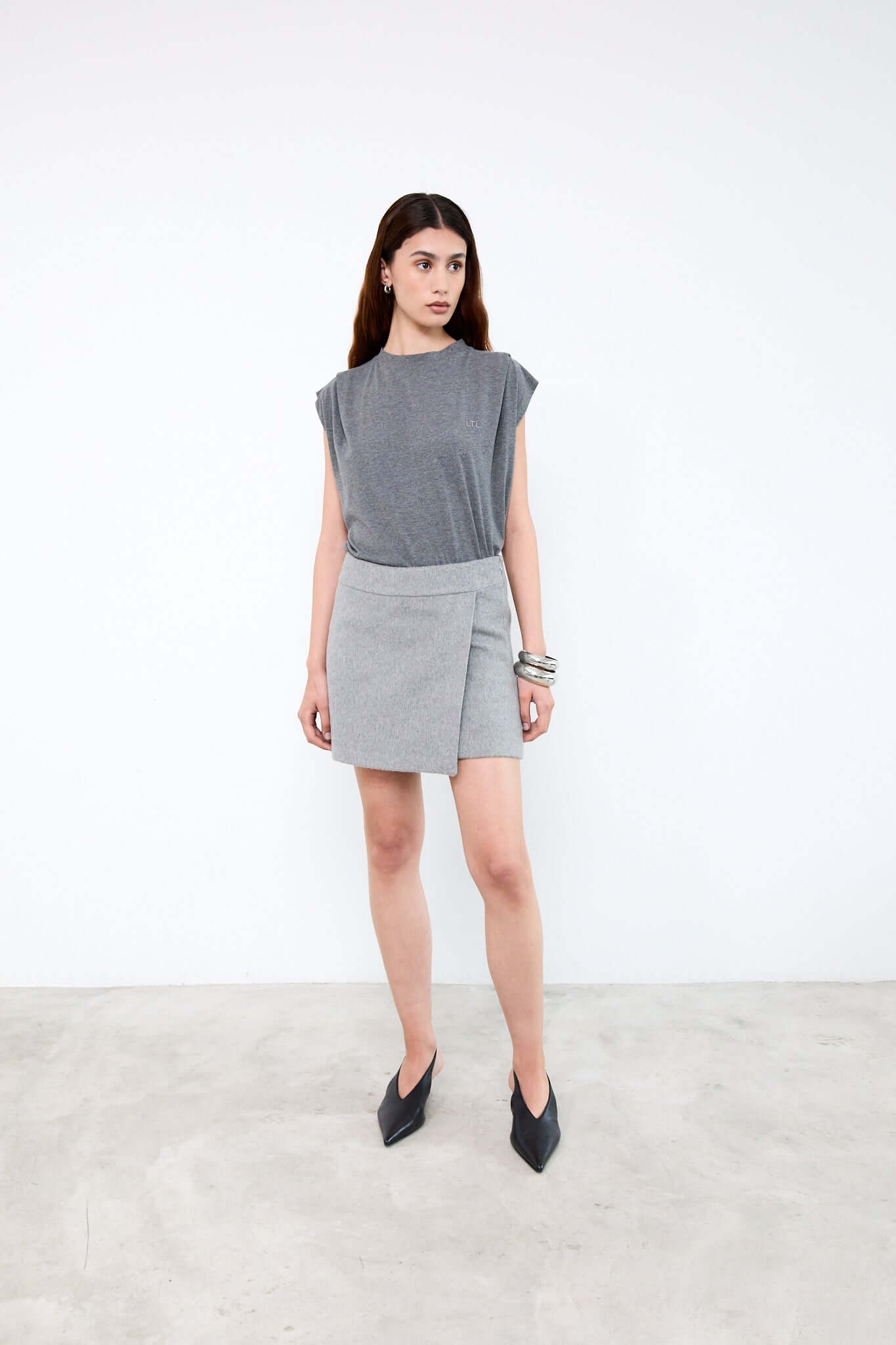 Woman wearing a gray sleeveless top and skirt with black shoes