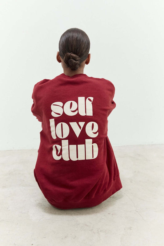 Person wearing a red sweatshirt with 'self love club' text on the back.