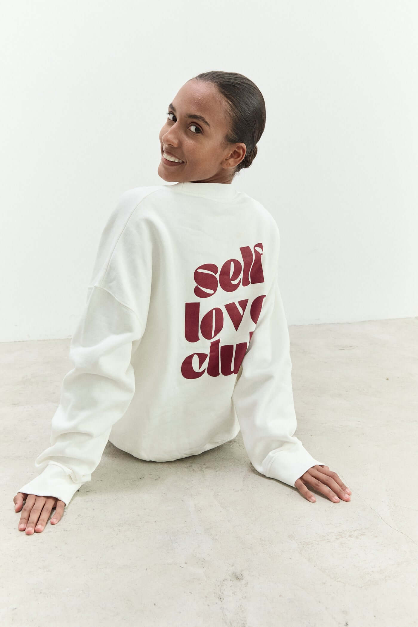 Person wearing a white sweatshirt with 'self love club' text on a light background