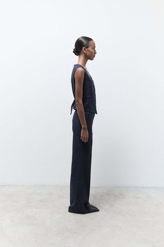 Person wearing a dark blue sleeveless top and pants standing against a white background