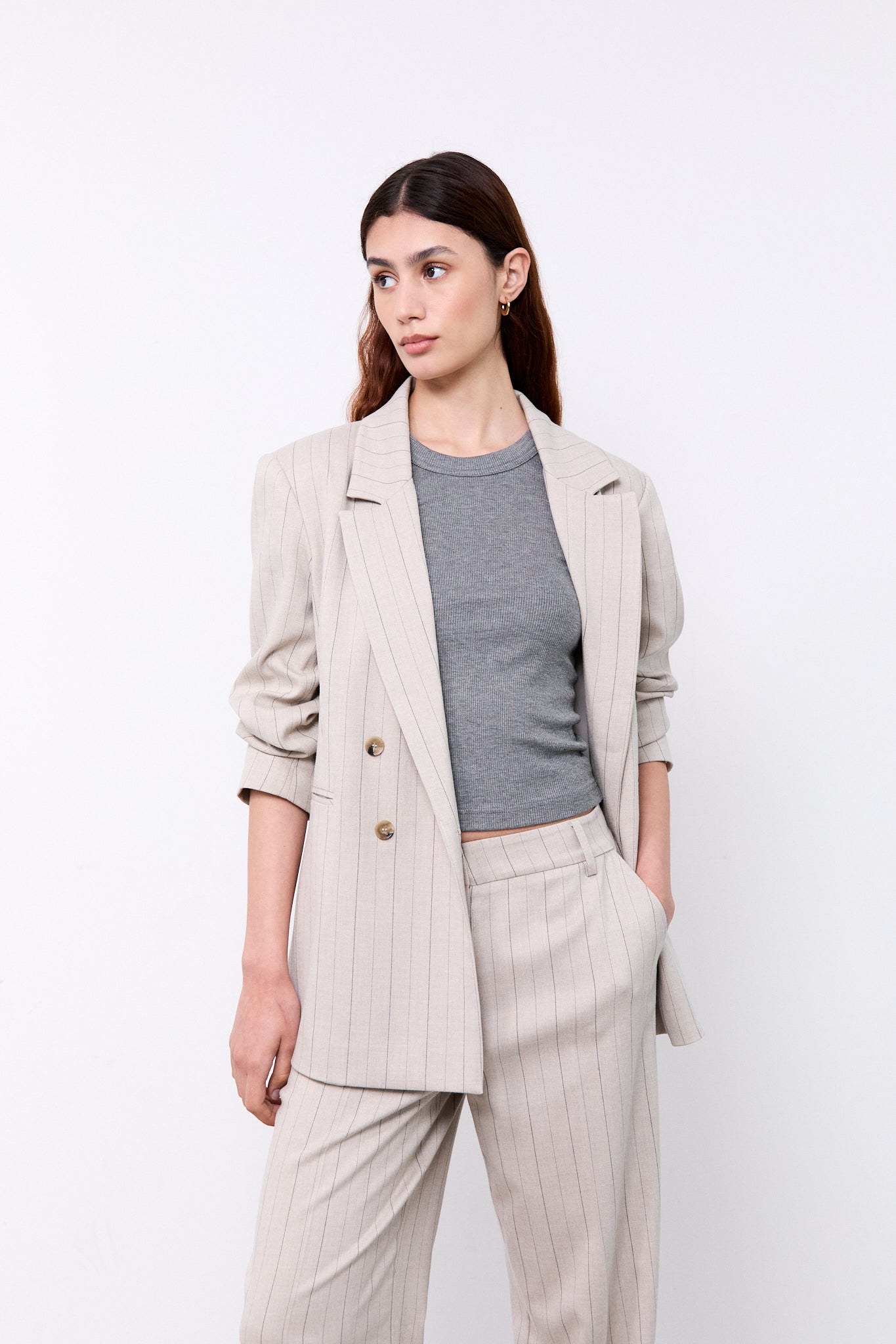 Woman wearing a beige blazer, gray top, and light-colored pants
