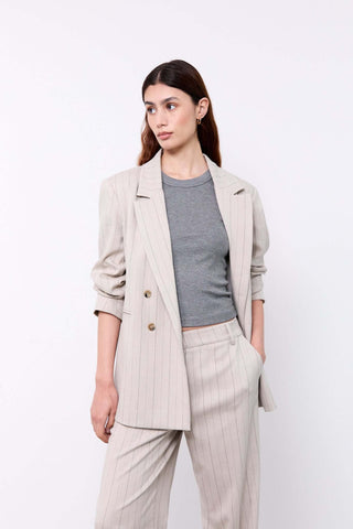 Woman wearing a beige blazer, gray top, and light-colored pants