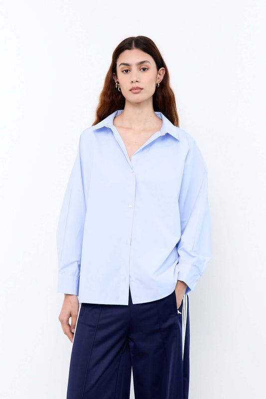 Woman wearing a light blue shirt and dark pants against a white background