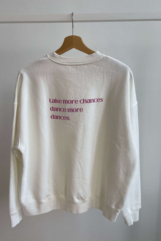 A white sweatshirt with the text 'Take more chances, dance more dances' printed