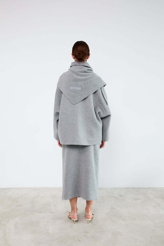 Person wearing a gray coat and skirt set against