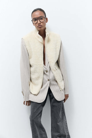 Person wearing a cream-colored jacket with fur collar against a white background