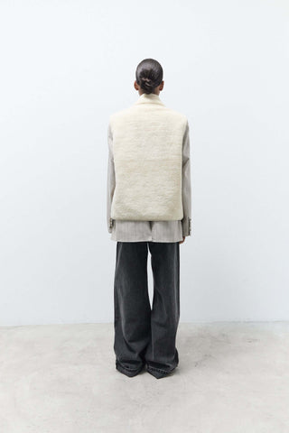 Person wearing a light-colored vest over a gray outfit on a white background