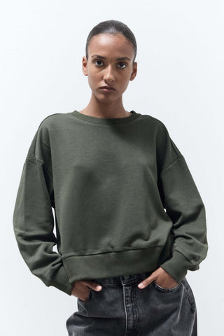 Person wearing a green sweatshirt and dark jeans on a light gray background