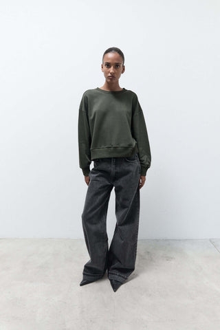 Person wearing a green sweater and black pants against a white background