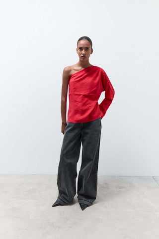 Person wearing a red one-shoulder top and gray pants against a white background