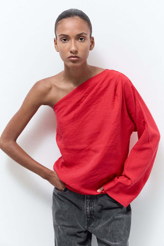 Person wearing a red one-shoulder top and gray pants on a white background