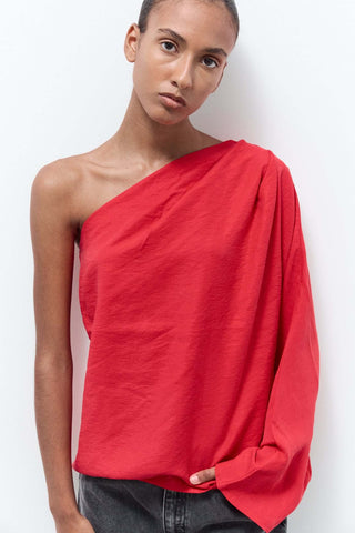 Model wearing a red one-shoulder top against a white background