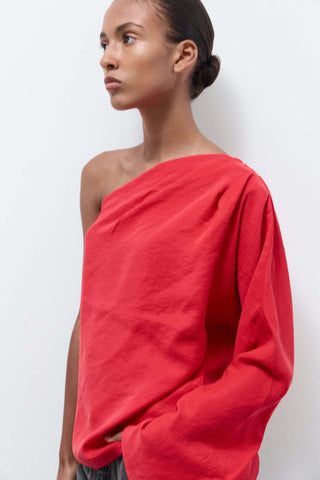 Woman wearing a red one-shoulder top against a white background