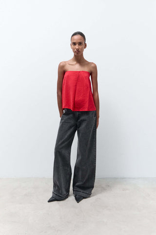 Woman wearing a strapless red top and dark jeans on a white background