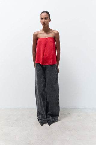 Woman wearing a red strapless top and black wide-leg pants on a white background