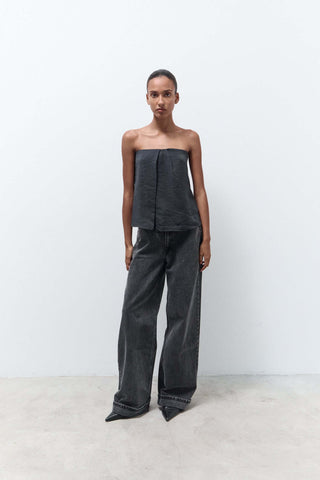 Woman wearing a dark gray strapless top and wide-leg pants against a white background