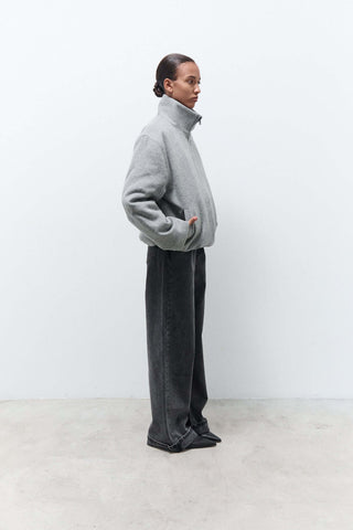 Person wearing a gray sweater and dark pants against a white background