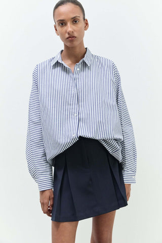 Woman wearing a blue and white striped shirt and navy skirt 