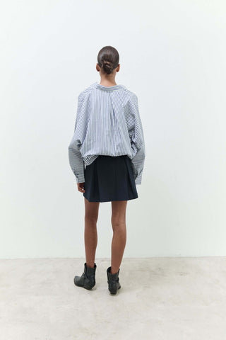 Person wearing a striped shirt and black skirt standing against a white wall.