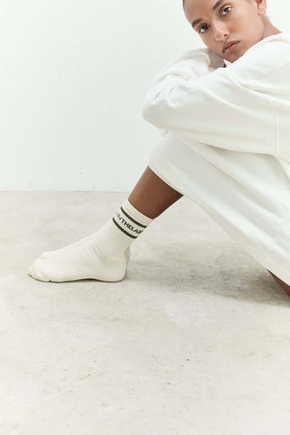 Person wearing white socks with text sitting on a light-colored floor.