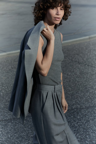 Woman in a gray outfit holding a jacket on a street.