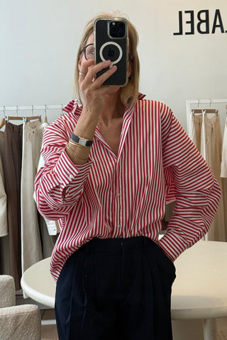 Person wearing a red and white striped shirt taking a mirror selfie in a clothing store.