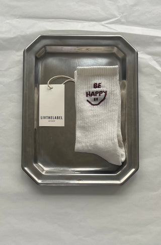 White sock with 'Be Happy' text on a silver tray, branded 'LIVTHELABEL'.