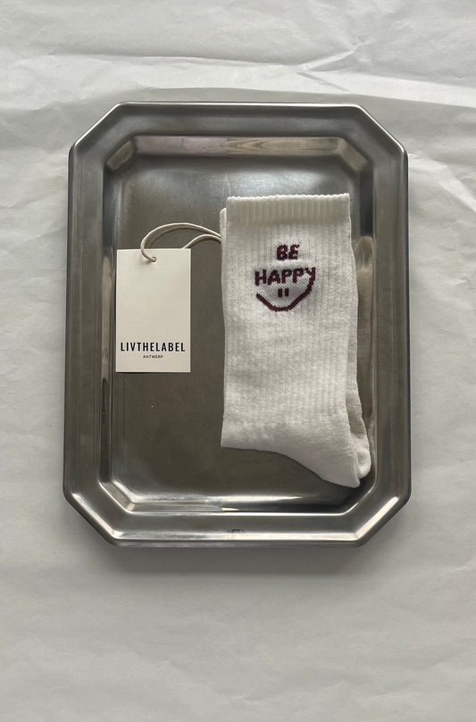 White sock with 'Be Happy' text on a silver tray, branded 'LIVTHELABEL'.