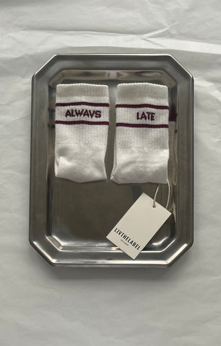 Two pairs of socks labeled 'Always' and 'Late' on a metallic tray with a tag.