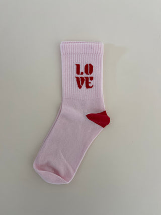 A pair of pink socks with the word 'LOVE' written on the side in a red heart symbol, and a small red mark on the heel.