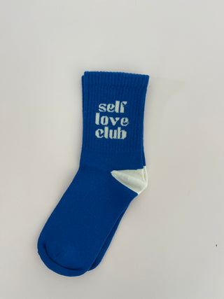 A blue sock with the text 'SELF LOVE CLUB' written on it, positioned against a white background.