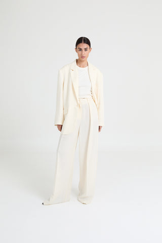 Person wearing a long cream coat and pants on a white background