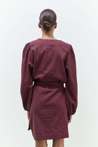 Person wearing a burgundy dress with long sleeves on a white background