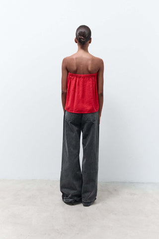 Person wearing a strapless red top and dark pants against a white background