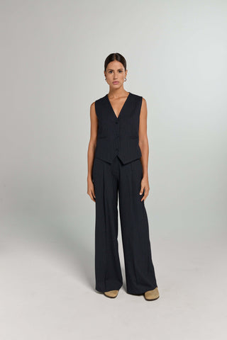 A model wearing a sleeveless navy top with a round neckline and matching navy pants with a pinstripe pattern. 