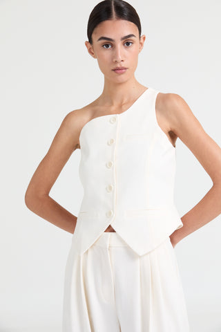 Woman wearing a white one-shoulder top with buttons on a plain background