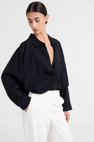 Woman wearing a black blouse with a deep neckline and white pants on a white background